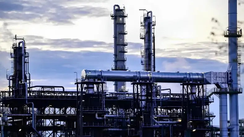 Tall steel distillation columns connected by overhead pipes at a refinery plant during twilight hours