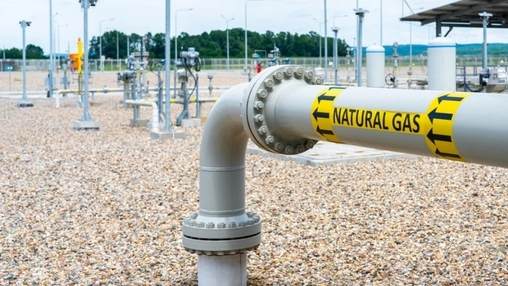 A large pipe labeled Natural Gas with yellow warning tape connects to a bolted flange fitting on gravel