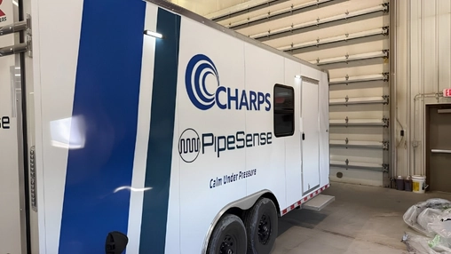 A large white utility trailer with Charps and PipeSense logos parked inside an industrial warehouse garage