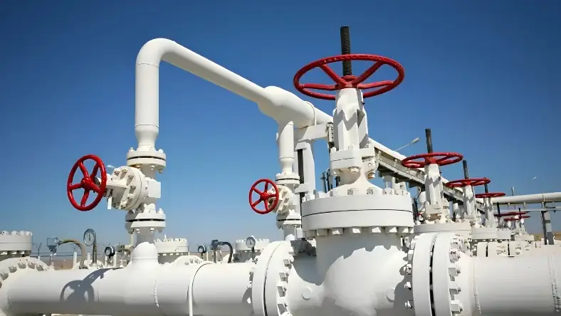 Close-up of white gas pipeline infrastructure with multiple red valve handwheels against a bright blue sky