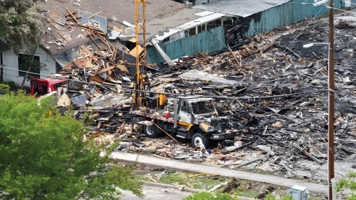Aerial view of a collapsed building site with scattered debris, a utility truck, and a mounted crane