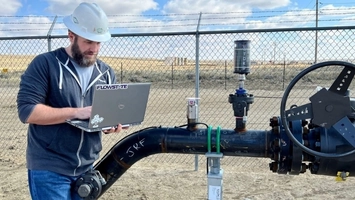 Engineer with a Flowstate laptop inspecting a pipeline valve and instrumentation at a rural field site
