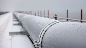Snow-dusted pipeline stretching into the foggy distance beside a metal guardrail with red safety markers