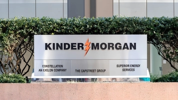 Kinder Morgan sign flanked by tenant company names, set against green hedges and a glass building facade