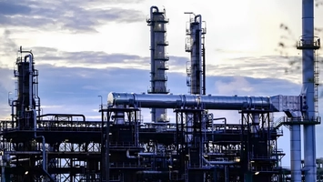 Tall steel distillation columns connected by overhead pipes at a refinery plant during twilight hours