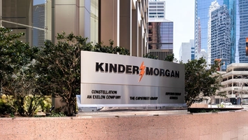 Metal Kinder Morgan corporate sign surrounded by shrubs with glass office towers in the background here
