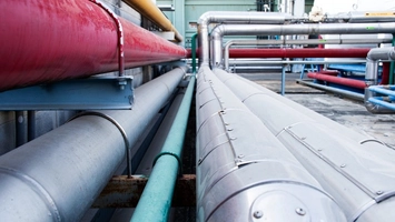 Silver insulated pipelines stretch alongside red and teal pipes at a large industrial processing site