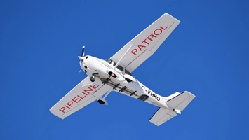 A small white patrol aircraft banks against a clear blue sky, marked with pipeline patrol lettering