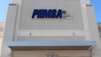 An exterior building sign reads PHMSA Training and Qualifications Center above a covered walkway entrance