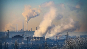 An industrial skyline with tall chimneys releasing dense smoke over frosted trees and rooftops below