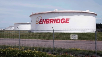 White oil storage tanks branded Enbridge behind a chain link fence with wildflowers in the foreground